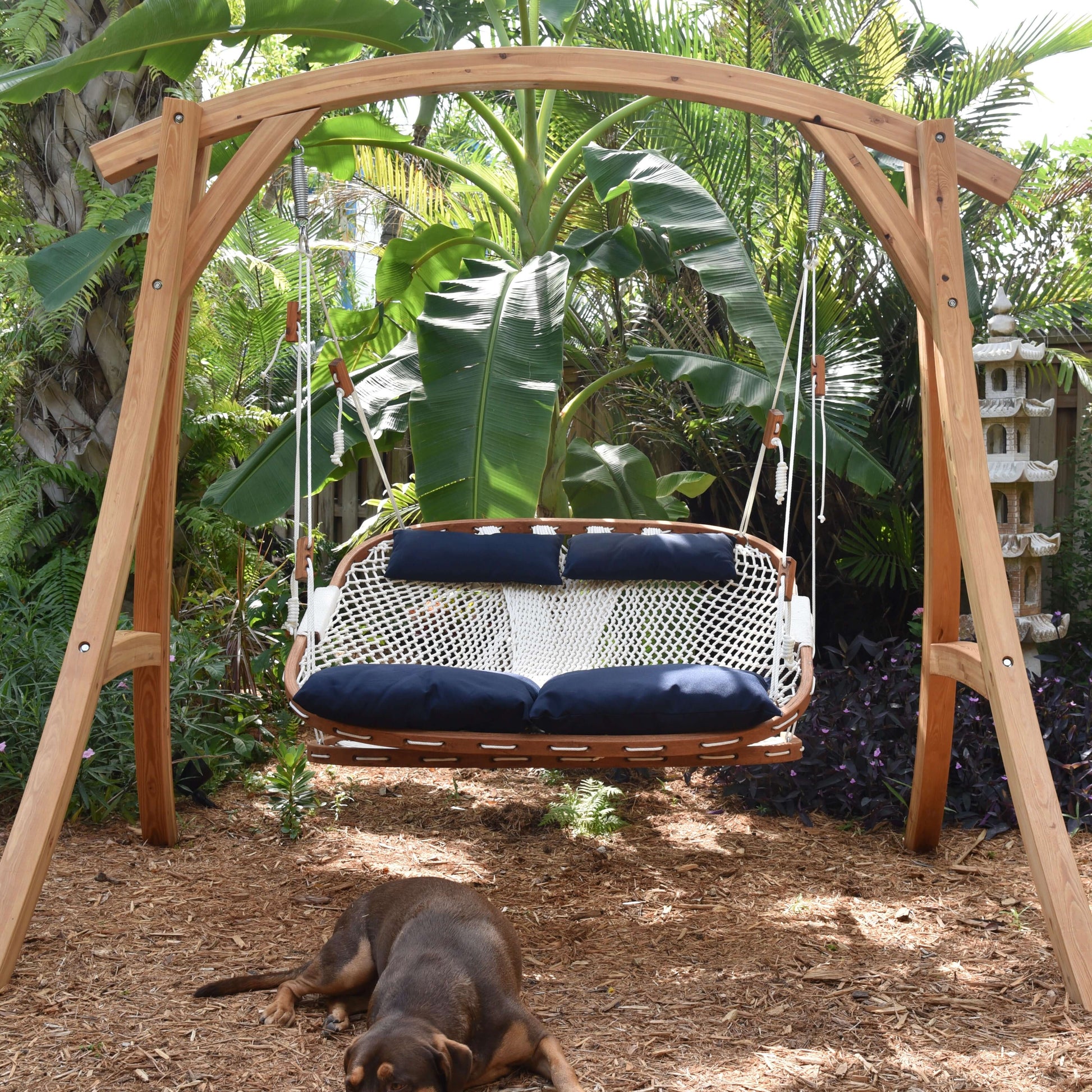 a dog laying in front of a hammock porch swing and stand in a key west garden