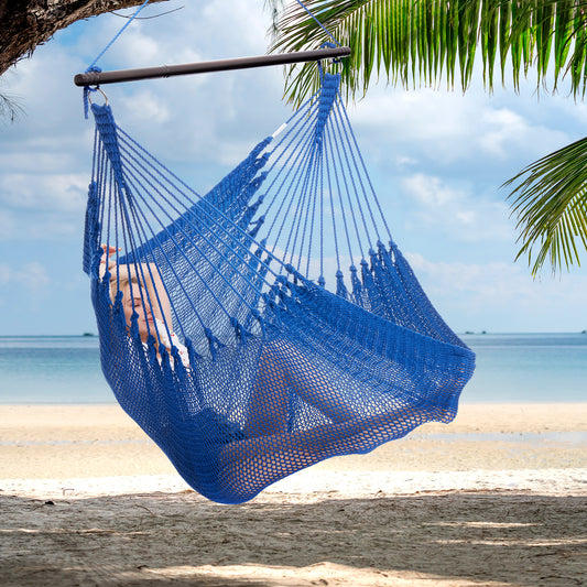 Person reclining in a dark blue Jumbo Caribbean Hammock Chair hung from a palm tree above a white sand beach