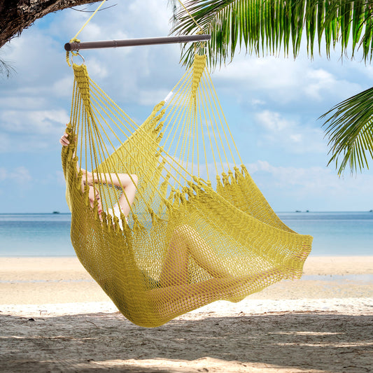 Person reclining in an olive Jumbo Caribbean Hammock Chair hung from a palm tree above a white sand beach