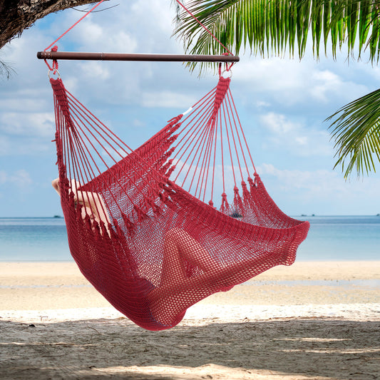 Person reclining in a red Jumbo Caribbean Hammock Chair hung from a palm tree above a white sand beach