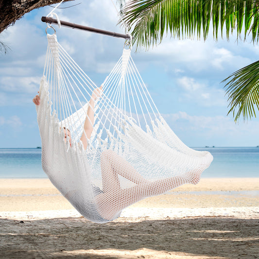 Person reclining in a white Jumbo Caribbean Hammock Chair hung from a palm tree above a white sand beach