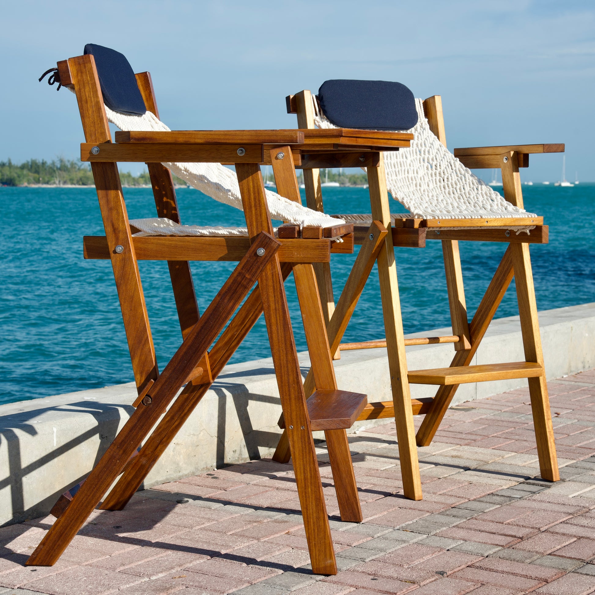 two wood bar stools with blue pillows by the ocean
