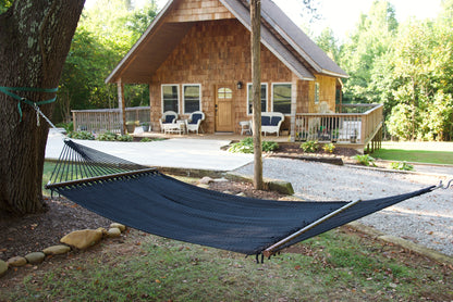 Black Double Caribbean Hammock hung between trees in front of a cedar-shingled cabin