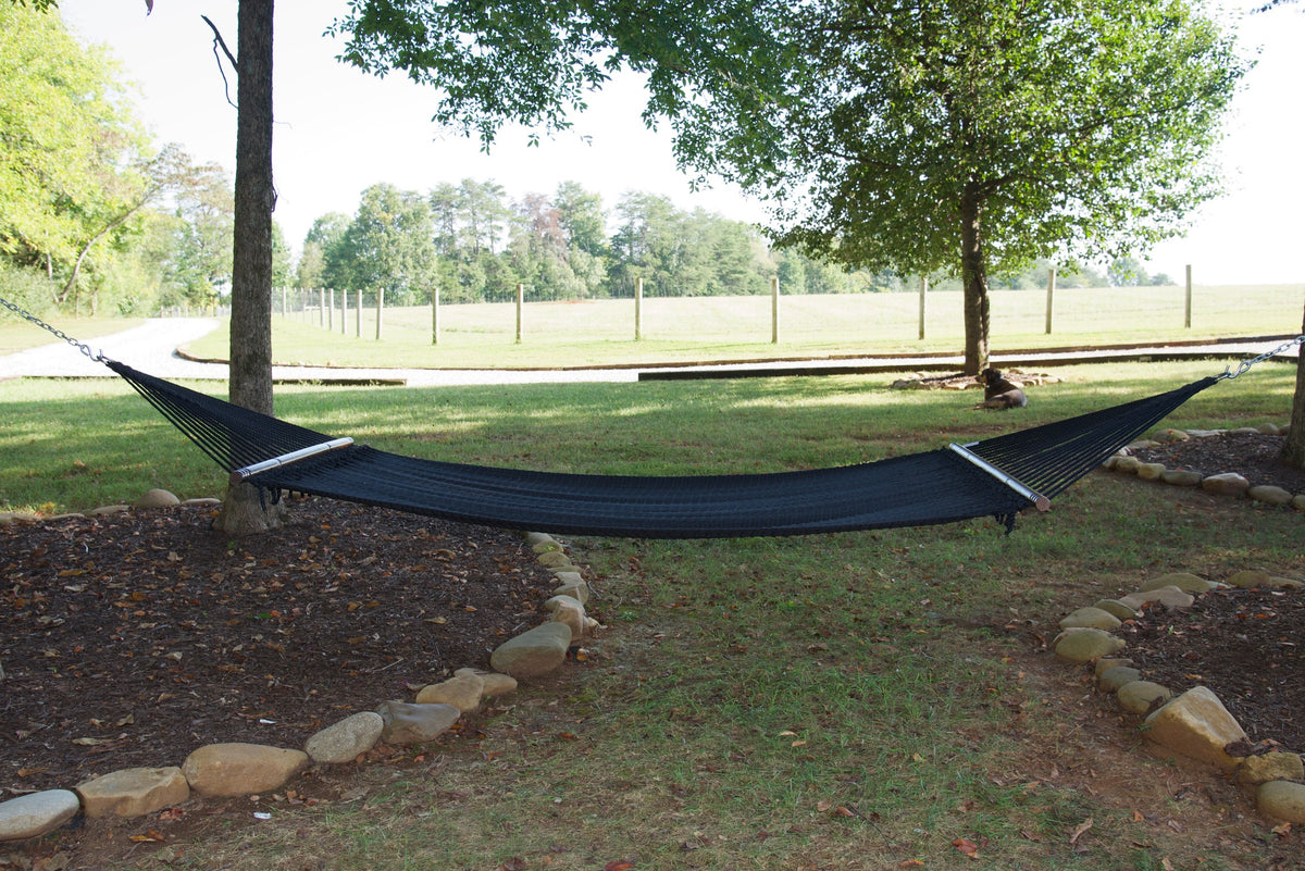 Black Double Caribbean Hammock hung between two trees in a backyard