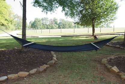 Black Double Caribbean Hammock hung between two trees in a backyard