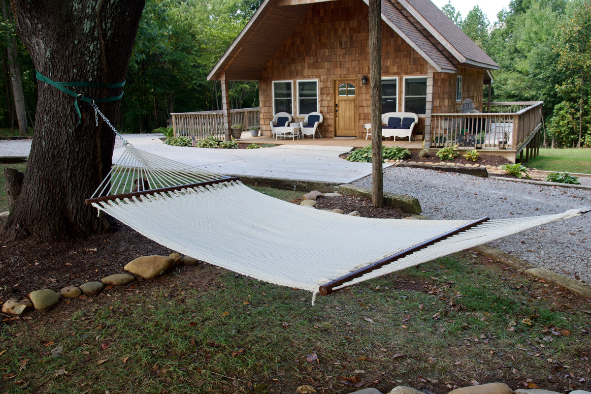 Cream Double Caribbean Hammock hung between trees in front of a cedar-shingled cabin