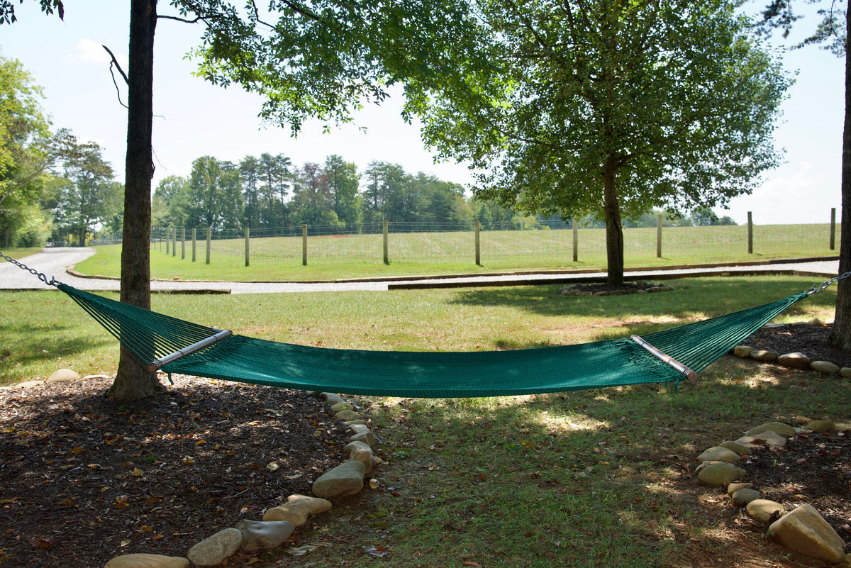 Green Double Caribbean Hammock hung between two trees in a backyard
