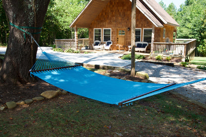 Light Blue Double Caribbean Hammock hung between trees in front of a cedar-shingled cabin