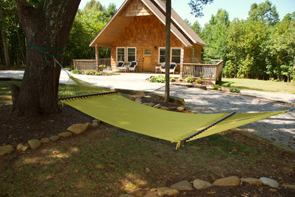 Olive Double Caribbean Hammock hung between trees in front of a cedar-shingled cabin