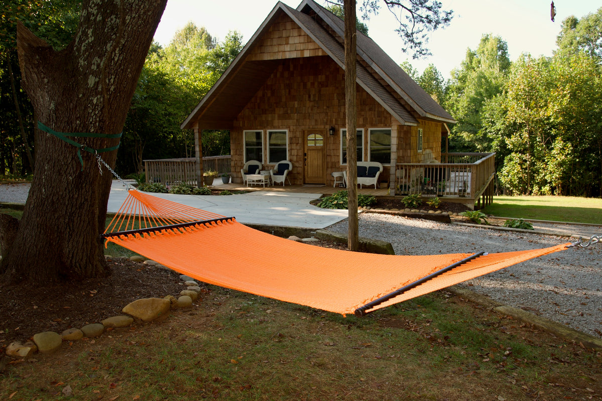 Orange Double Caribbean Hammock hung between trees in front of a cedar-shingled cabin