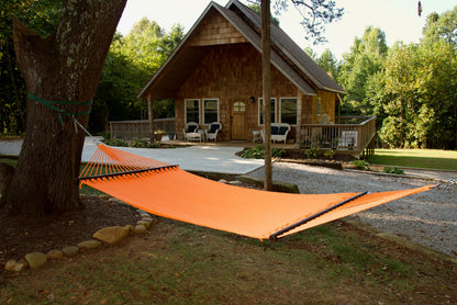 Orange Double Caribbean Hammock hung between trees in front of a cedar-shingled cabin