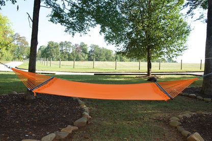Orange Double Caribbean Hammock hung between two trees in a backyard