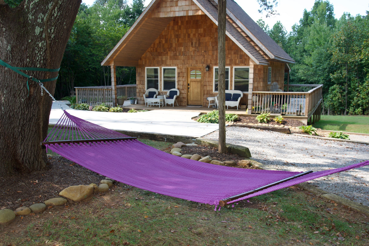 Purple Double Caribbean Hammock hung between trees in front of a cedar-shingled cabin