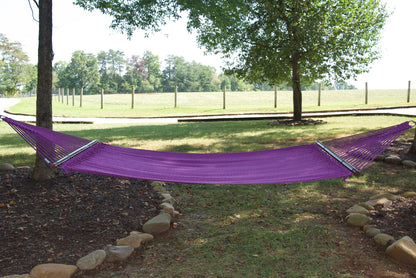 Purple Double Caribbean Hammock hung between two trees in a backyard