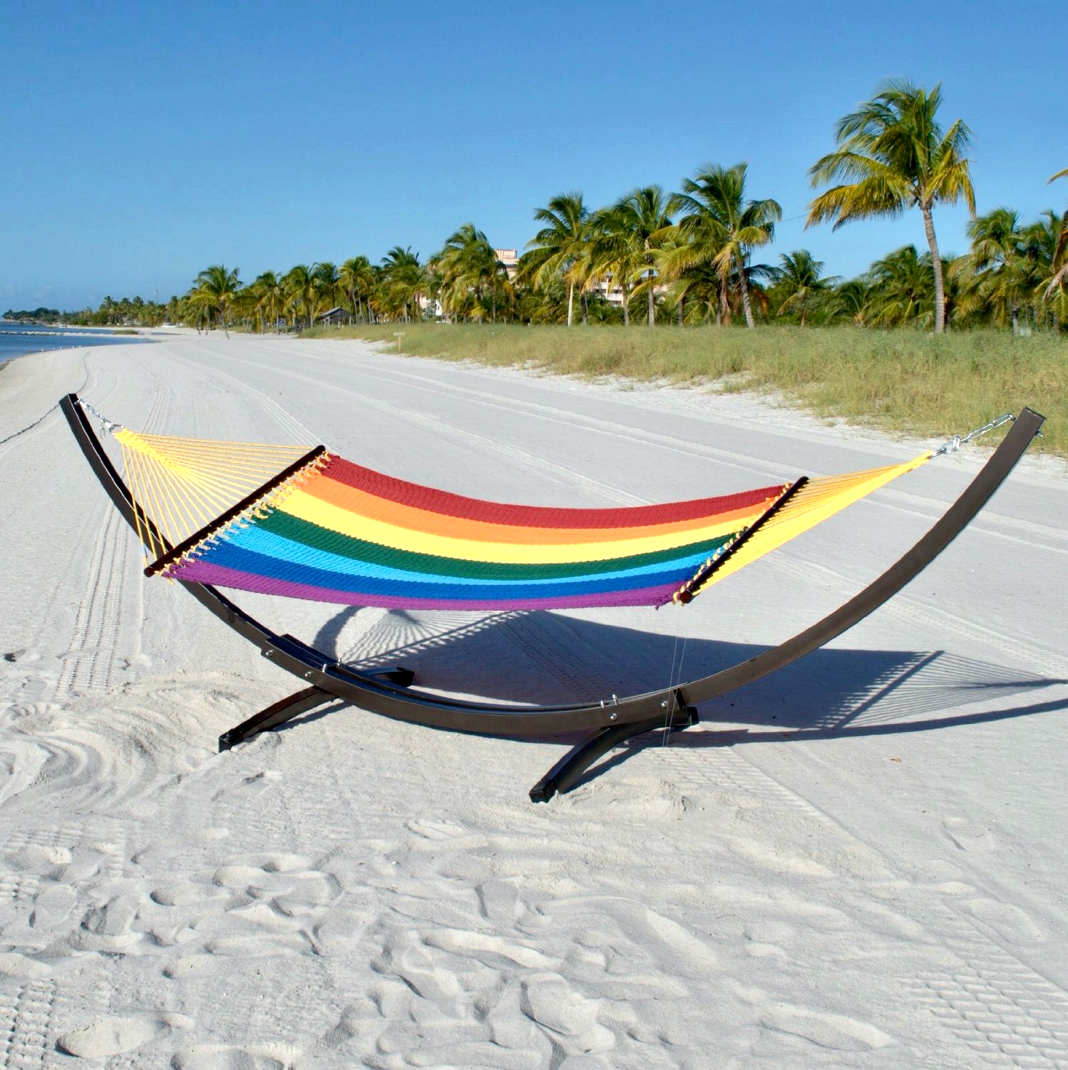 Rainbow Double Caribbean Hammock hanging on the Wood Arc Hammock Stand on a palm-lined beach