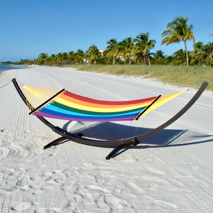 Rainbow Double Caribbean Hammock hanging on the Wood Arc Hammock Stand on a palm-lined beach