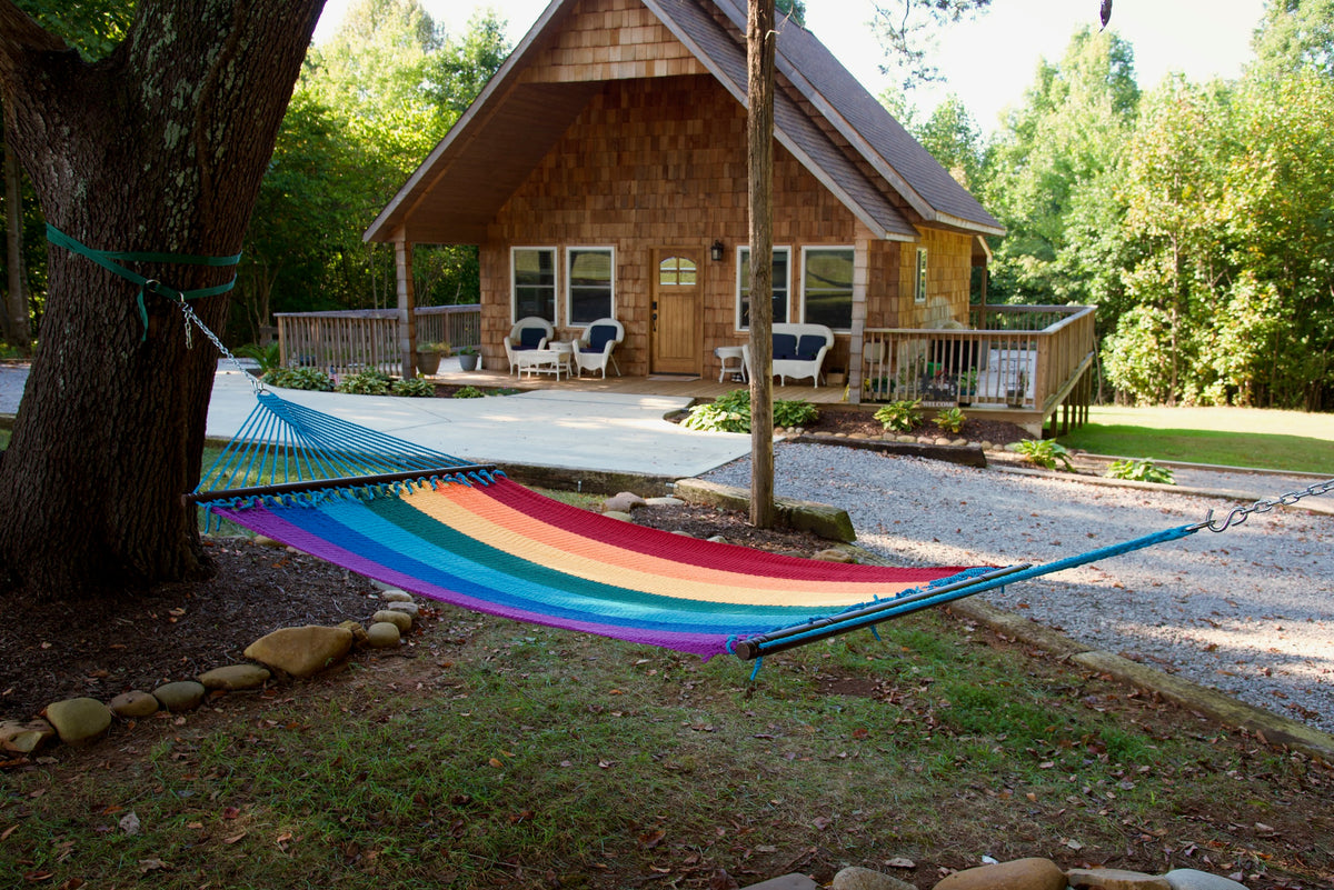 Rainbow Double Caribbean Hammock hung between trees in front of a cedar-shingled cabin