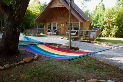 Rainbow Double Caribbean Hammock hung between trees in front of a cedar-shingled cabin