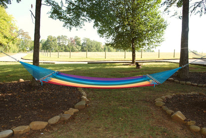 Rainbow Double Caribbean Hammock hung between two trees in a backyard