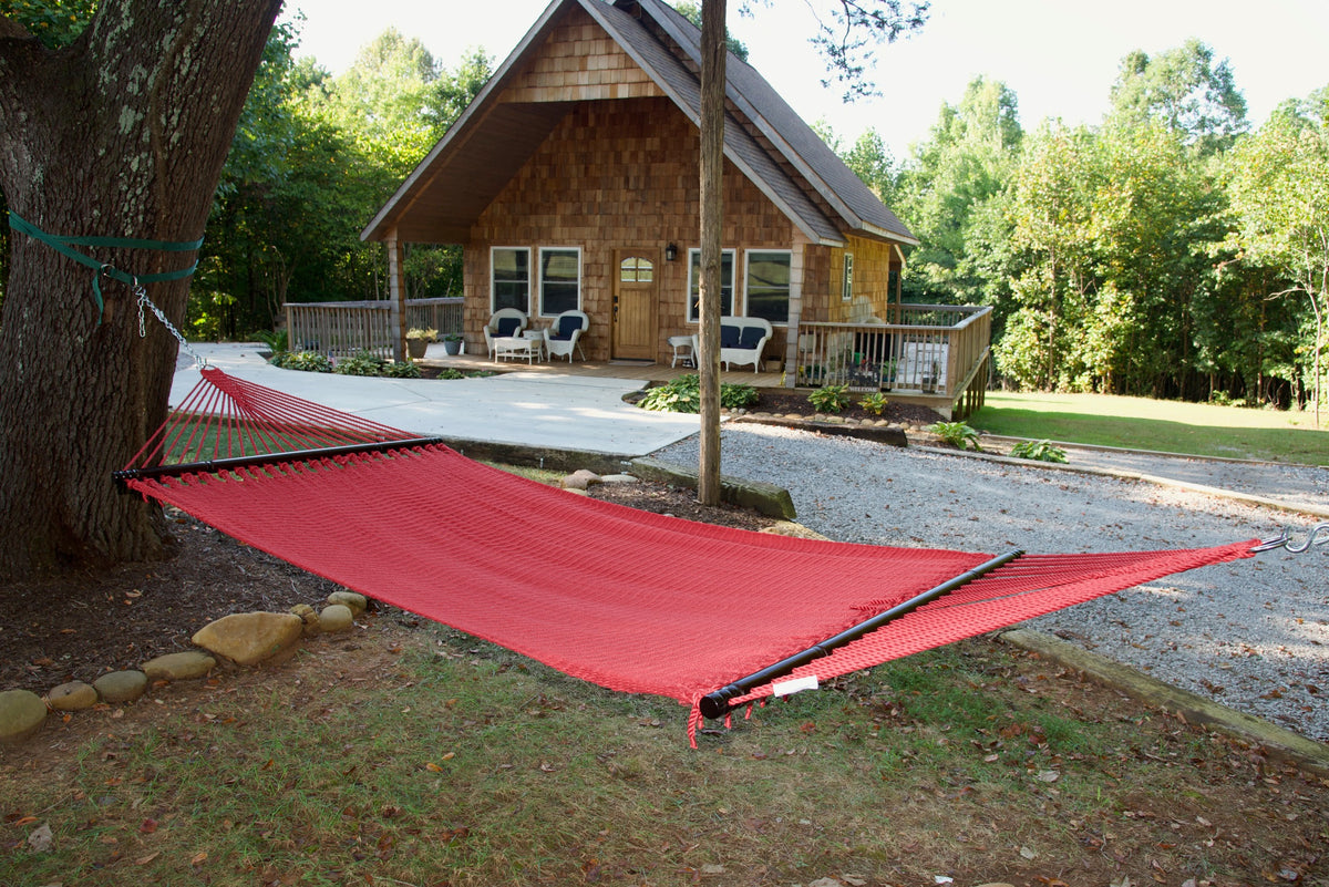 Red Double Caribbean Hammock hung between trees in front of a cedar-shingled cabin