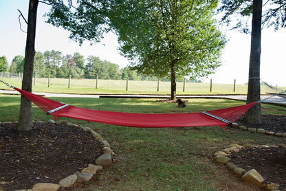 Red Double Caribbean Hammock hung between two trees in a backyard