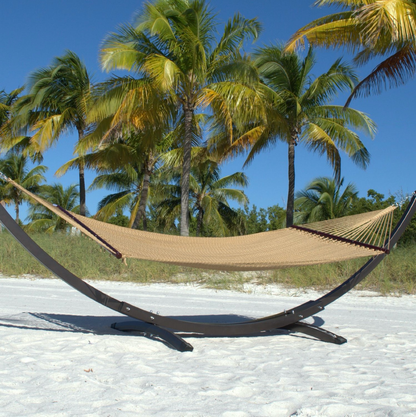 Tan Double Caribbean Hammock hanging on the Wood Arc Hammock Stand on a palm-lined beach