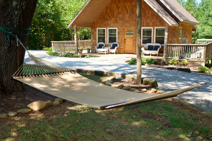 Tan Double Caribbean Hammock hung between trees in front of a cedar-shingled cabin