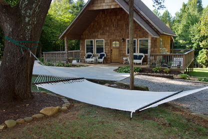 White Double Caribbean Hammock hung between trees in front of a cedar-shingled cabin