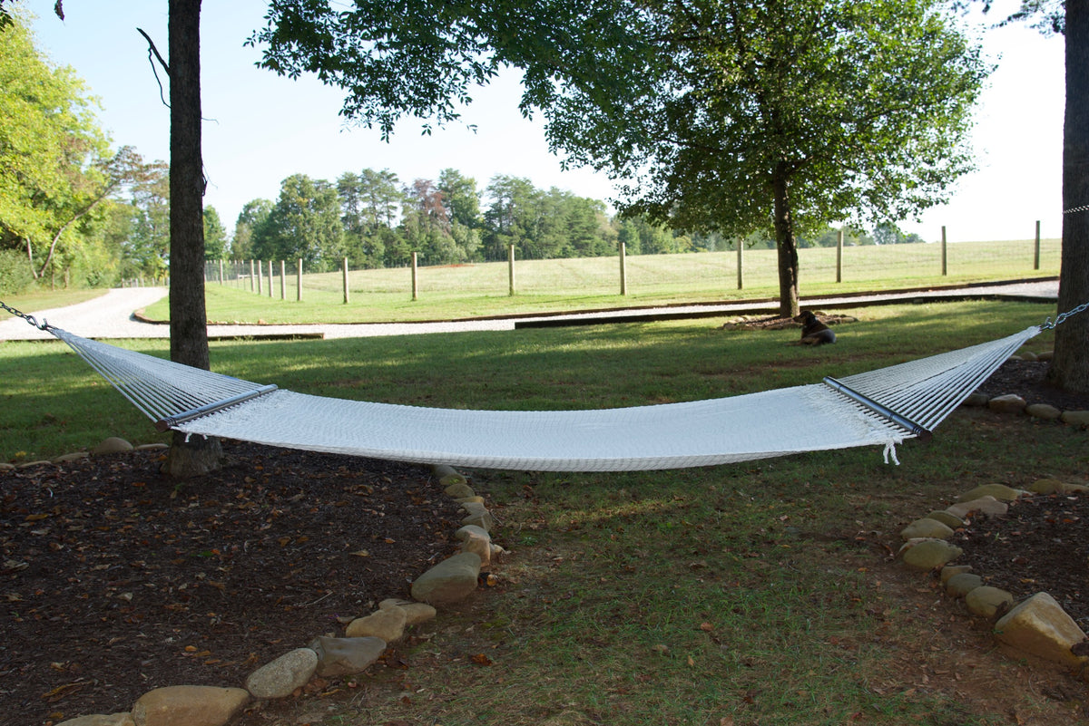 White Double Caribbean Hammock hung between two trees in a backyard