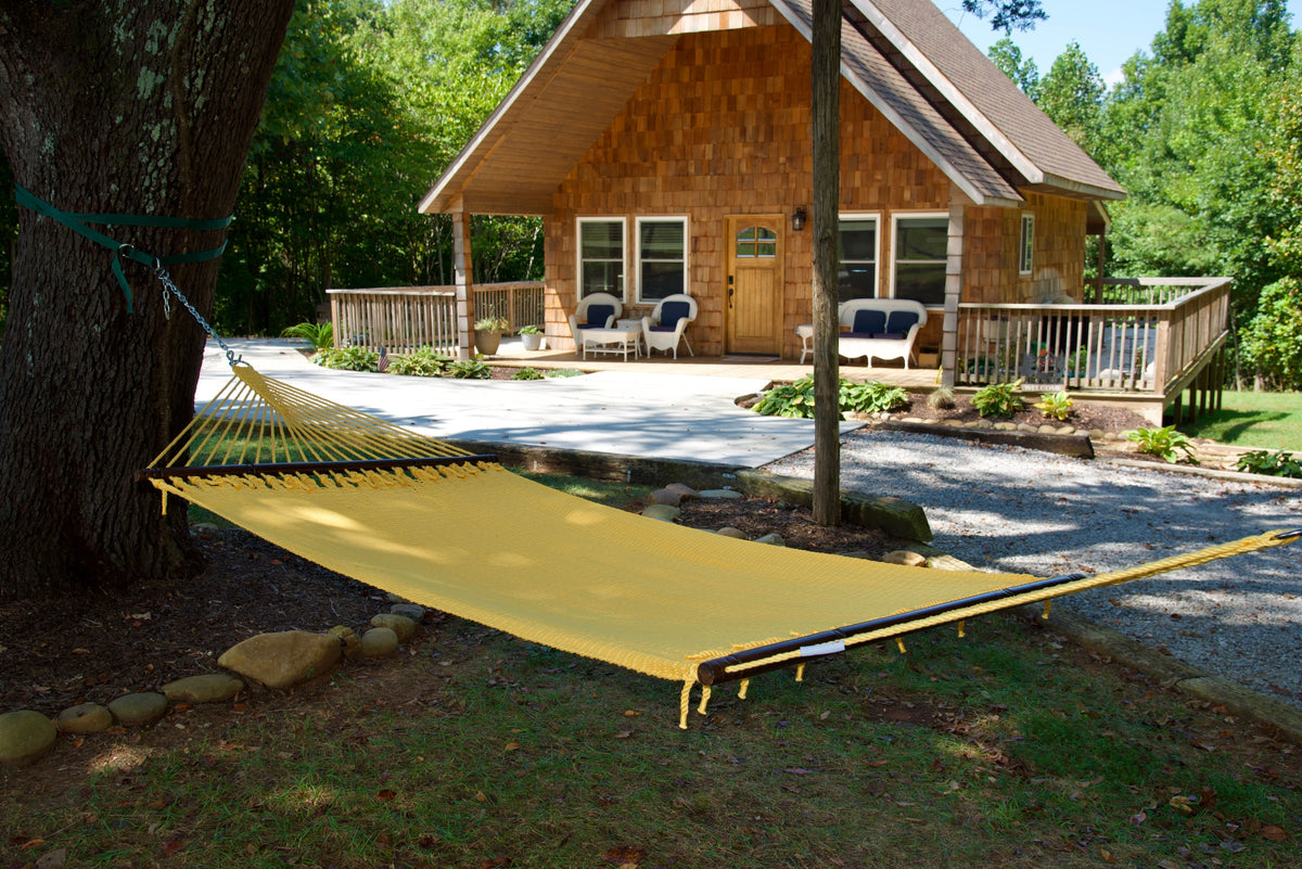 Yellow Double Caribbean Hammock hung between trees in front of a cedar-shingled cabin