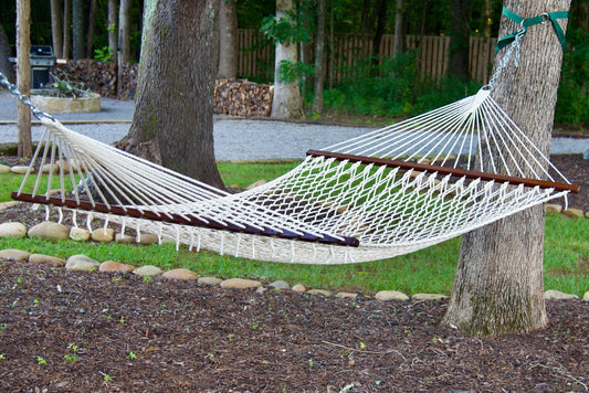 Cream Island Escape hammock hung between two trees above a stone-edged mulch bed