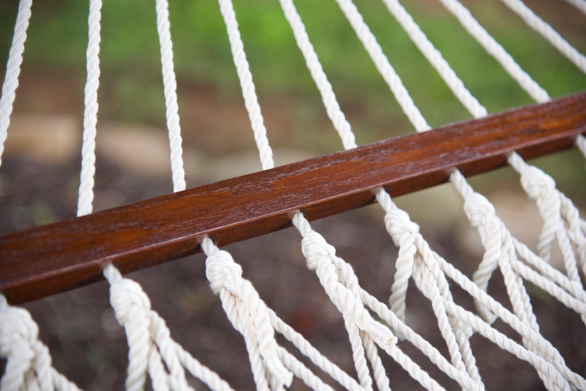 Close-up of the knotted polyester cord ends along the hardwood spreader bar of a cream Island Escape hammock
