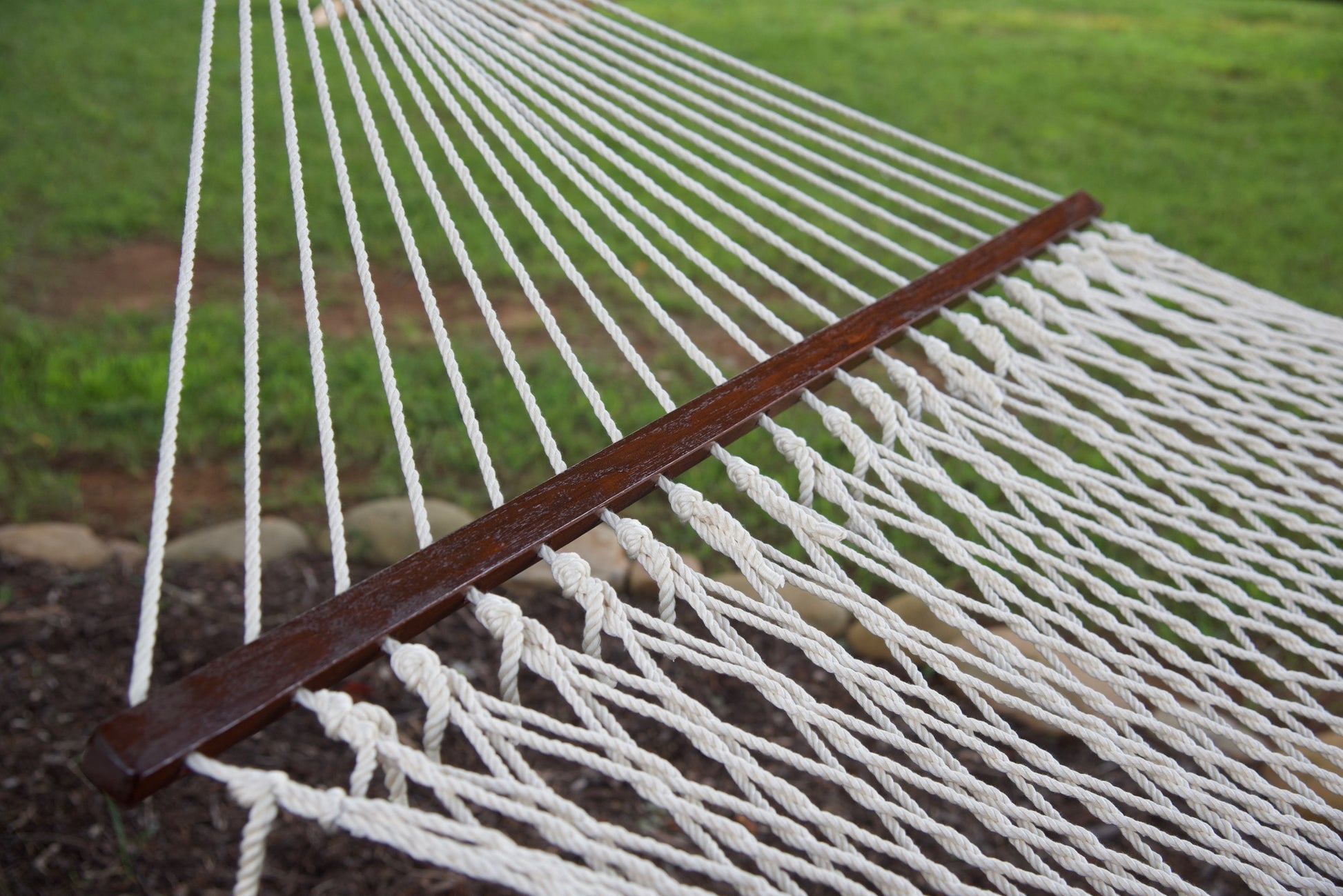 Open-weave polyester bed of a cream Island Escape hammock running to the hardwood spreader bar