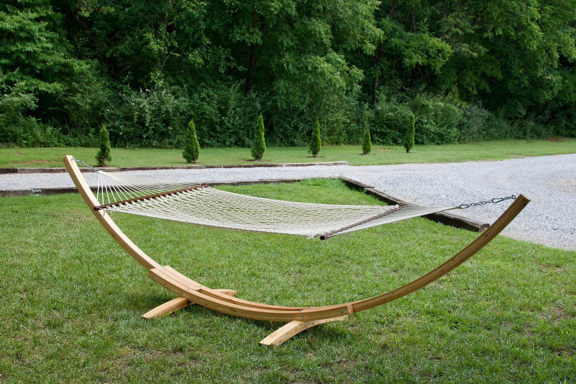 Cream Island Escape hammock hanging on the Wood Arc Hammock Stand on a lawn beside a gravel path