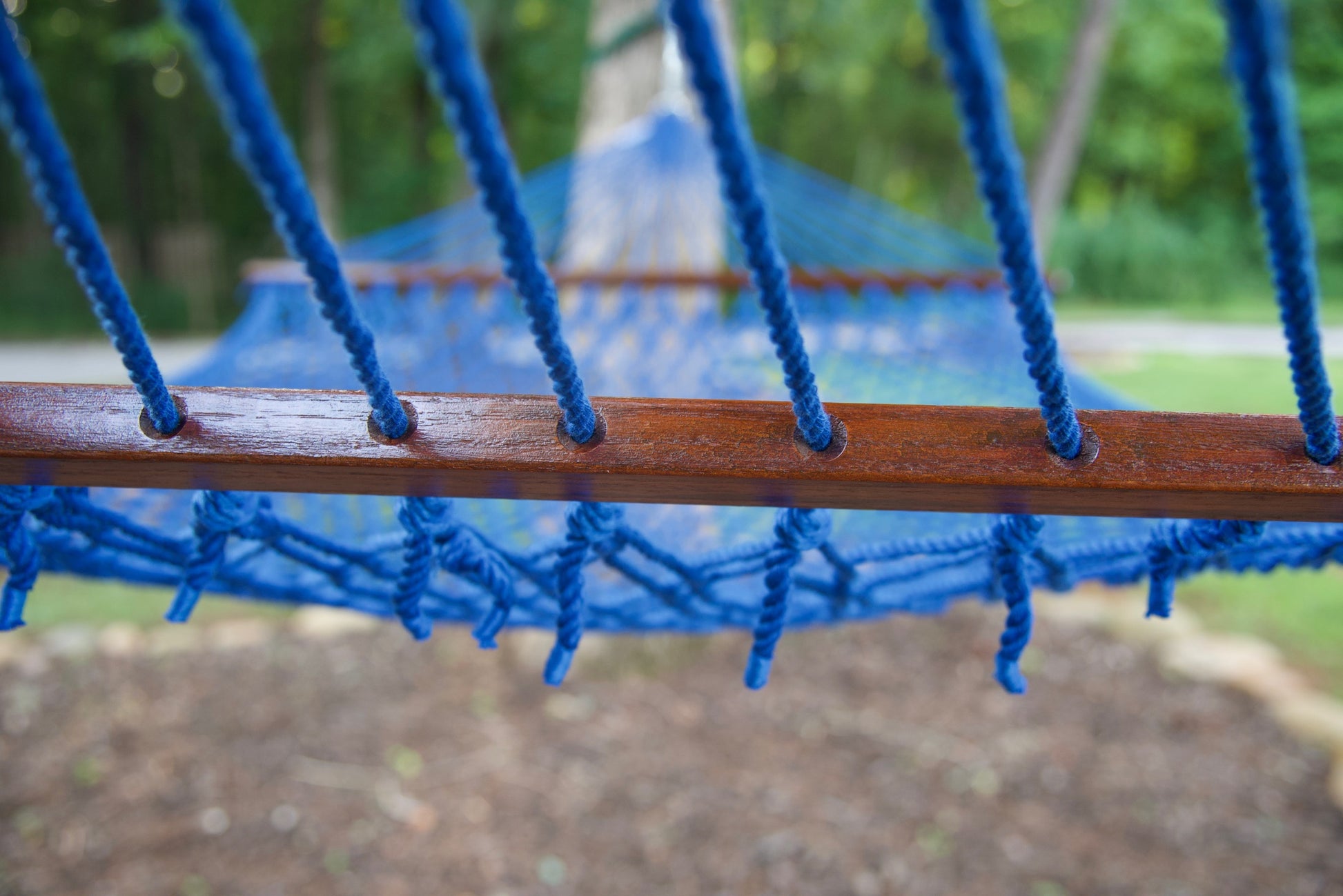 Polyester cords threaded through the drilled hardwood spreader bar of a dark blue Island Escape hammock