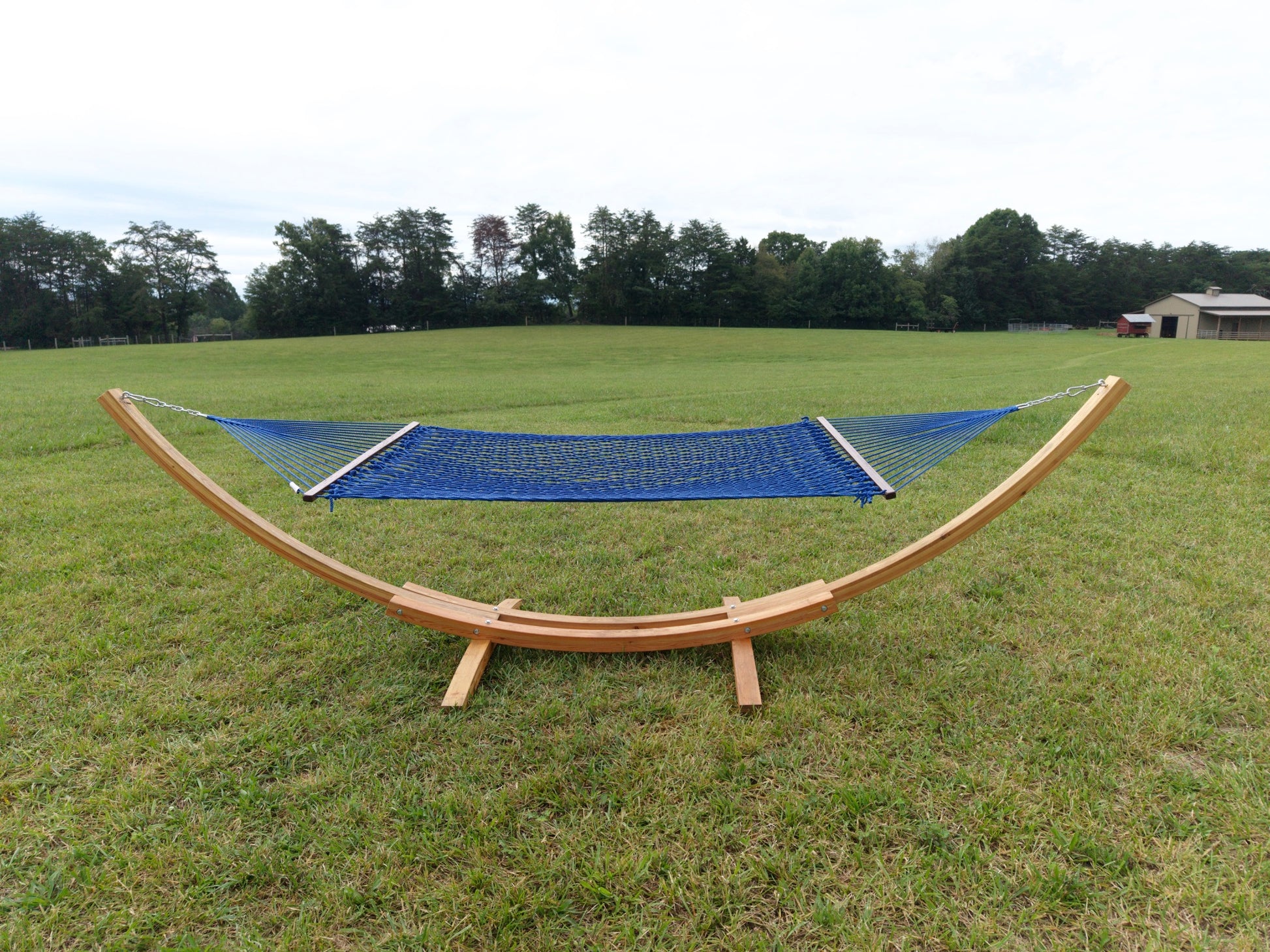 Dark blue Island Escape hammock hanging on the Wood Arc Hammock Stand in a mown field with a barn behind