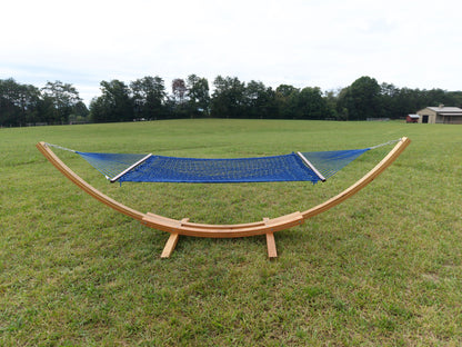 Dark blue Island Escape hammock hanging on the Wood Arc Hammock Stand in a mown field with a barn behind