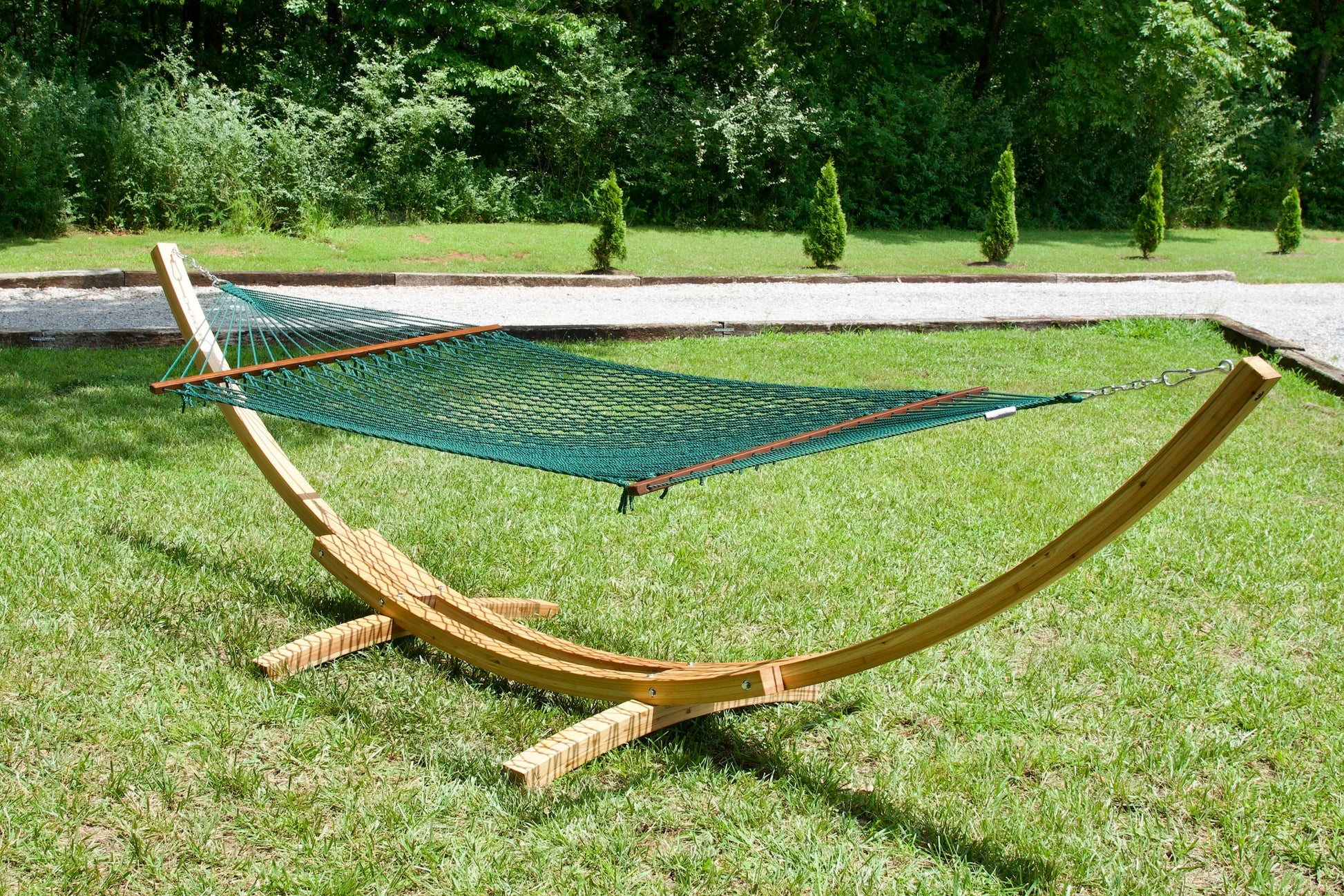 Green Island Escape hammock hanging on the Wood Arc Hammock Stand on a lawn beside a gravel path