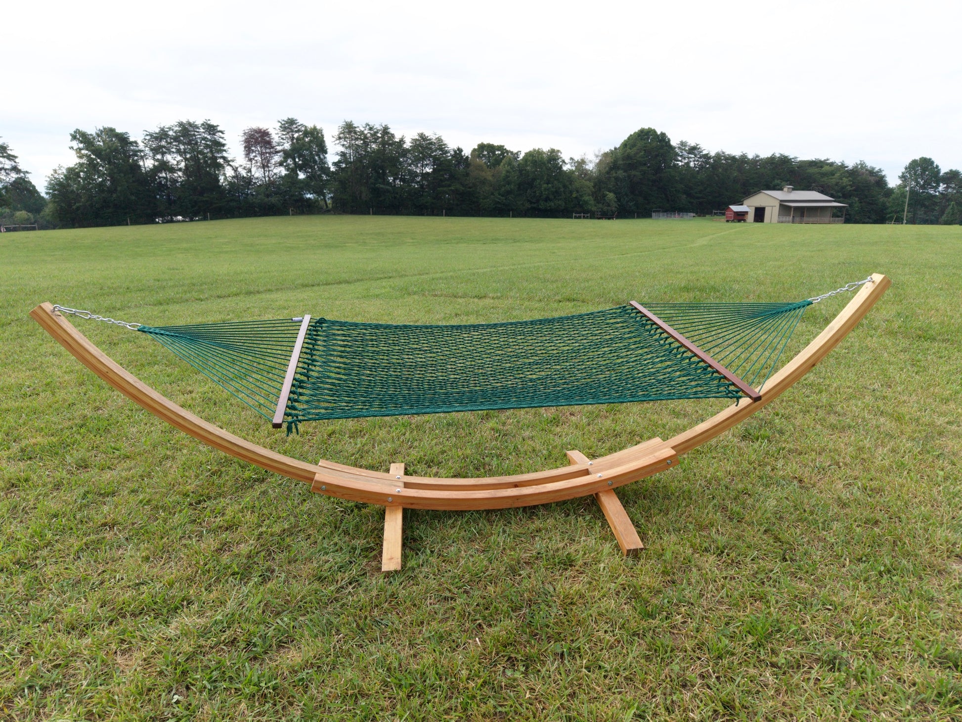 Green Island Escape hammock hanging on the Wood Arc Hammock Stand in a mown field with a barn behind