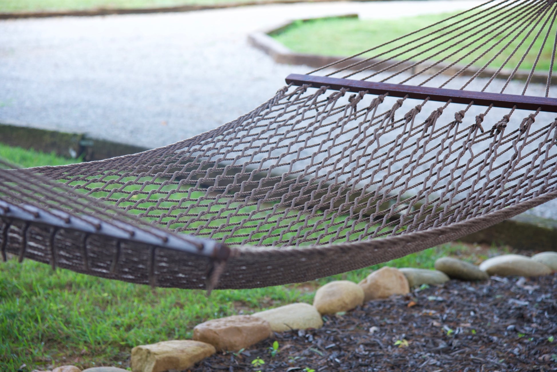 Side view of the open-weave polyester bed and hardwood spreader bar on a mocha Island Escape hammock, stone-edged bed and walkway behind