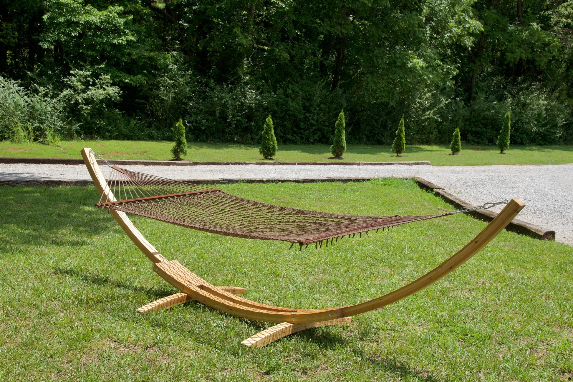 Mocha Island Escape hammock hanging on the Wood Arc Hammock Stand on a lawn beside a gravel path