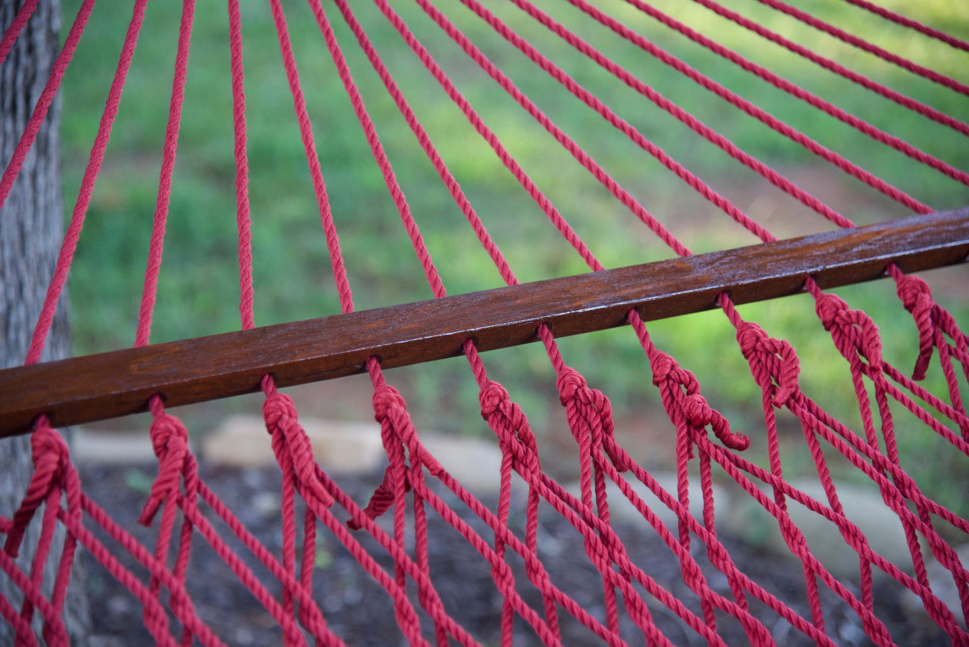 Close-up of the knotted polyester cord ends along the hardwood spreader bar of a red Island Escape hammock