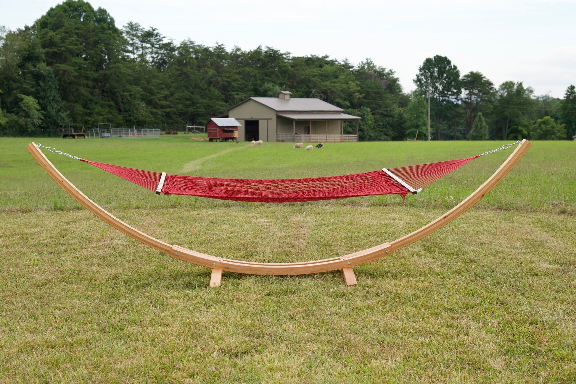 Red Island Escape hammock hanging on the Wood Arc Hammock Stand in a pasture with a barn behind