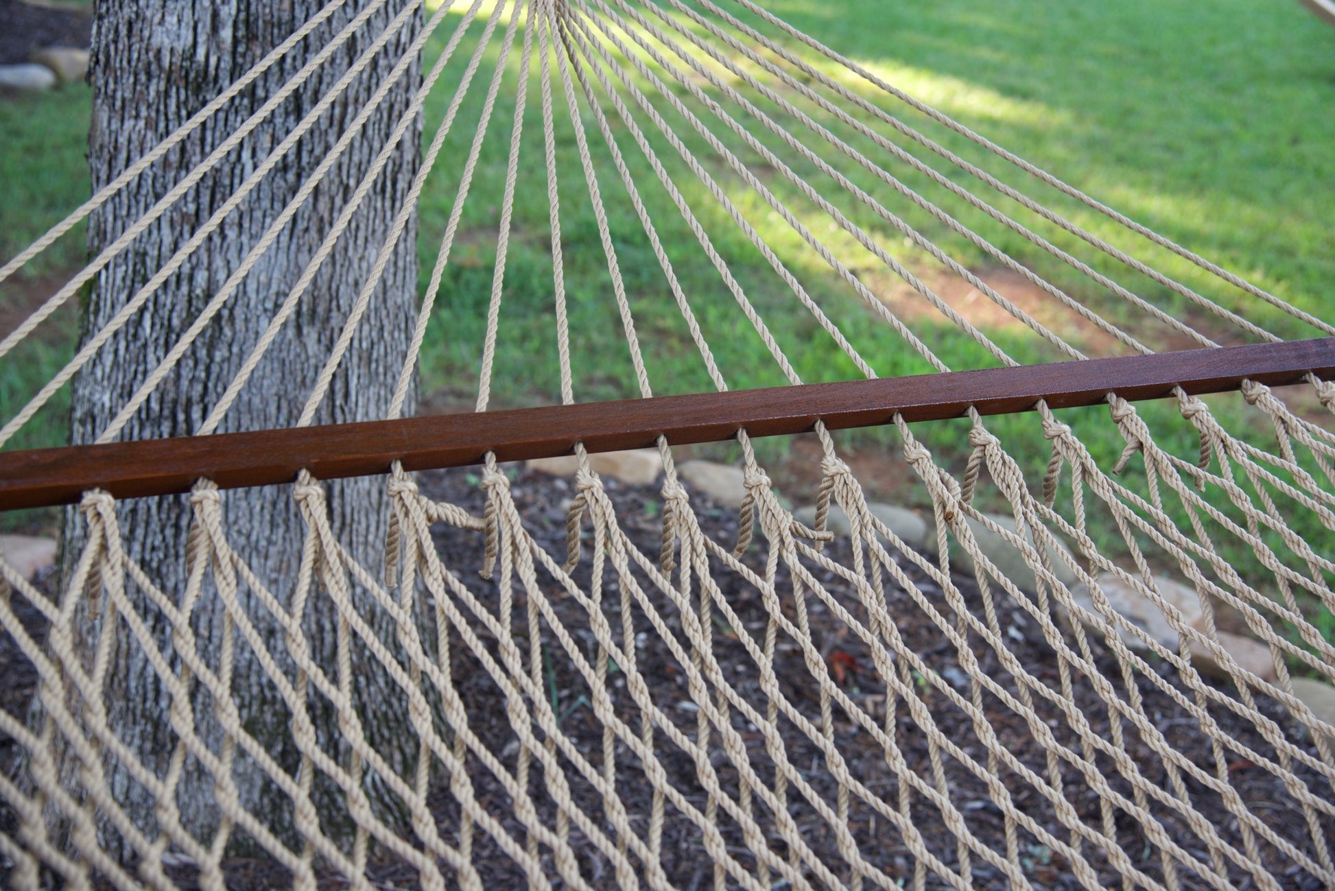 Hardwood spreader bar on a tan Island Escape hammock with knotted polyester cord ends, open weave above
