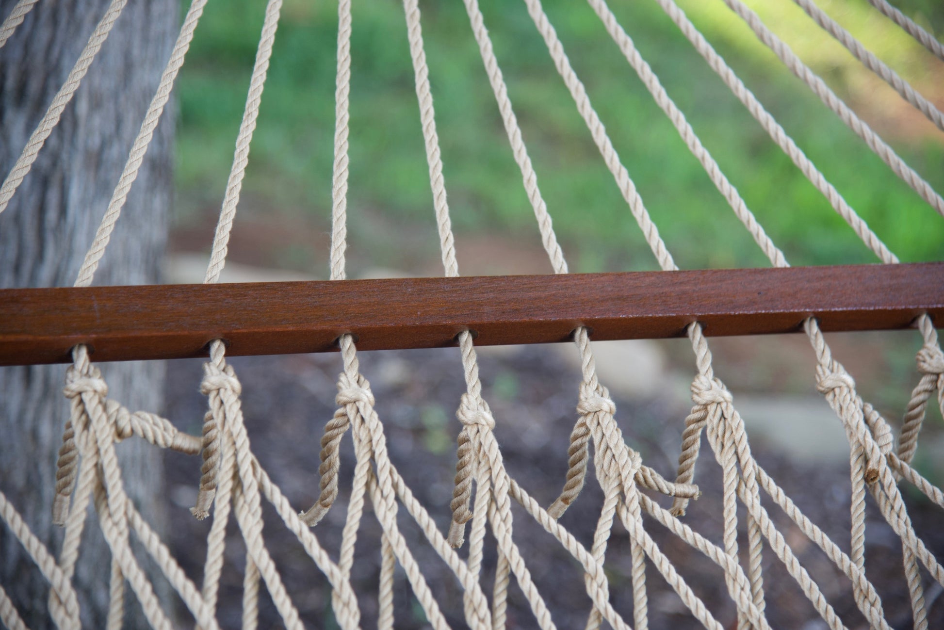 Close-up of the knotted polyester cord ends beneath the hardwood spreader bar of a tan Island Escape hammock