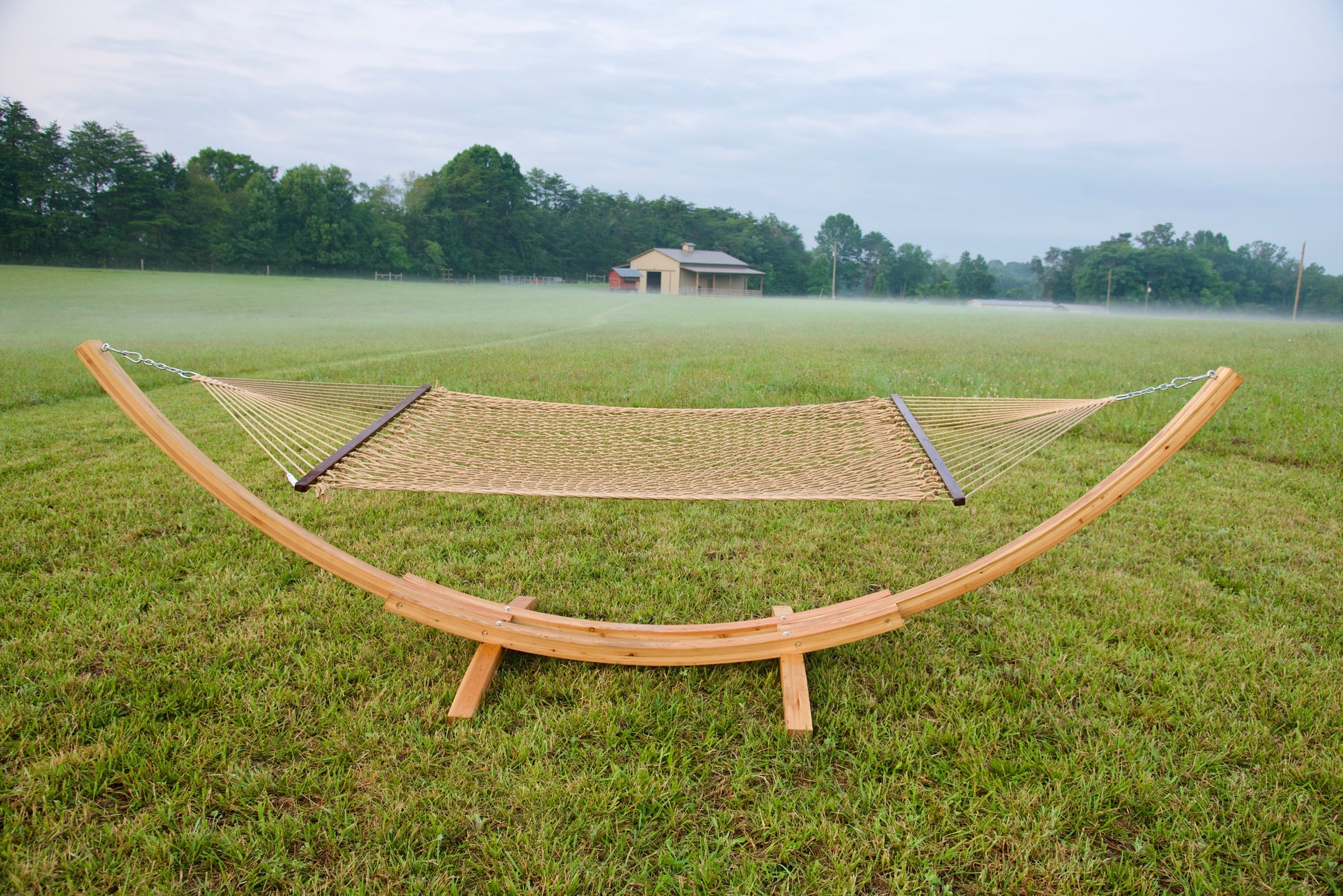Tan Island Escape hammock hanging on the Wood Arc Hammock Stand in a misty field with a barn behind