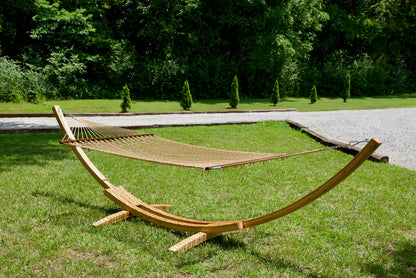 Tan Island Escape hammock hanging on the Wood Arc Hammock Stand on a lawn beside a gravel path