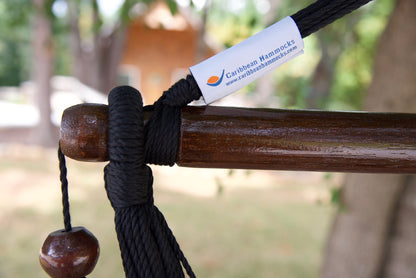 The dark varnished hardwood spreader bar of a black Island Haven hammock chair, with end cords looped over it and a wooden bead hanging below