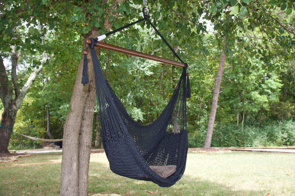 Black Island Haven hammock chair with a brown seat pillow, hanging from a tree in a wooded backyard with a timber cabin behind