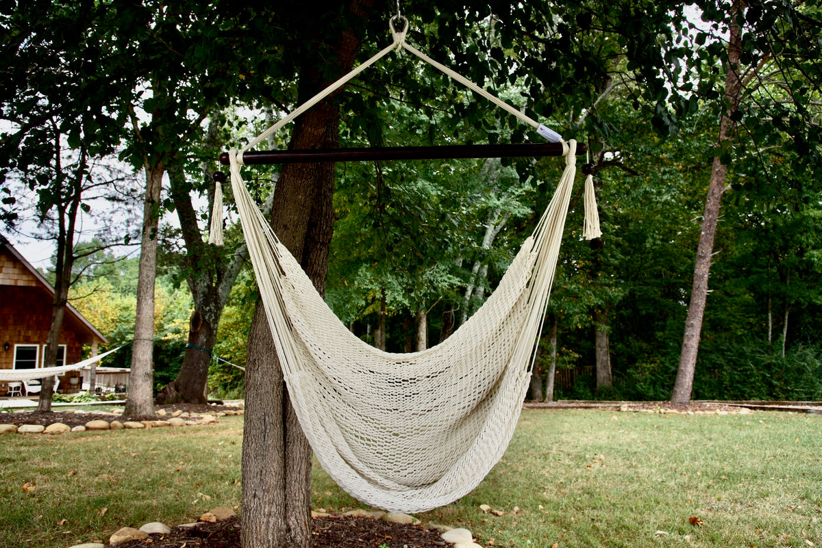 Cream Island Haven hammock chair hanging from a shade tree in a mown backyard with woods behind